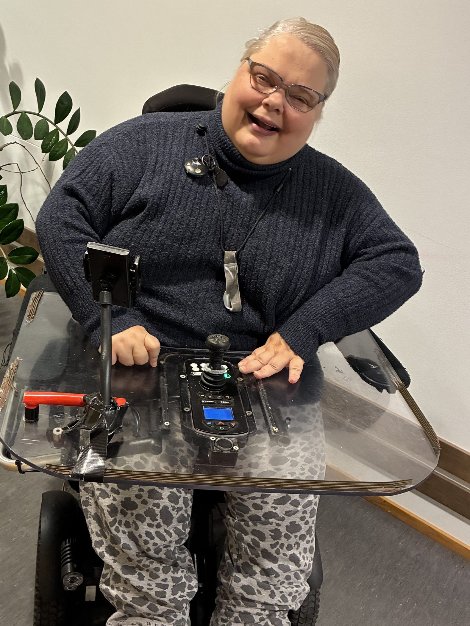 Marju istuu sähköpyörätuolissa ja katsoo hymyillen kameraa