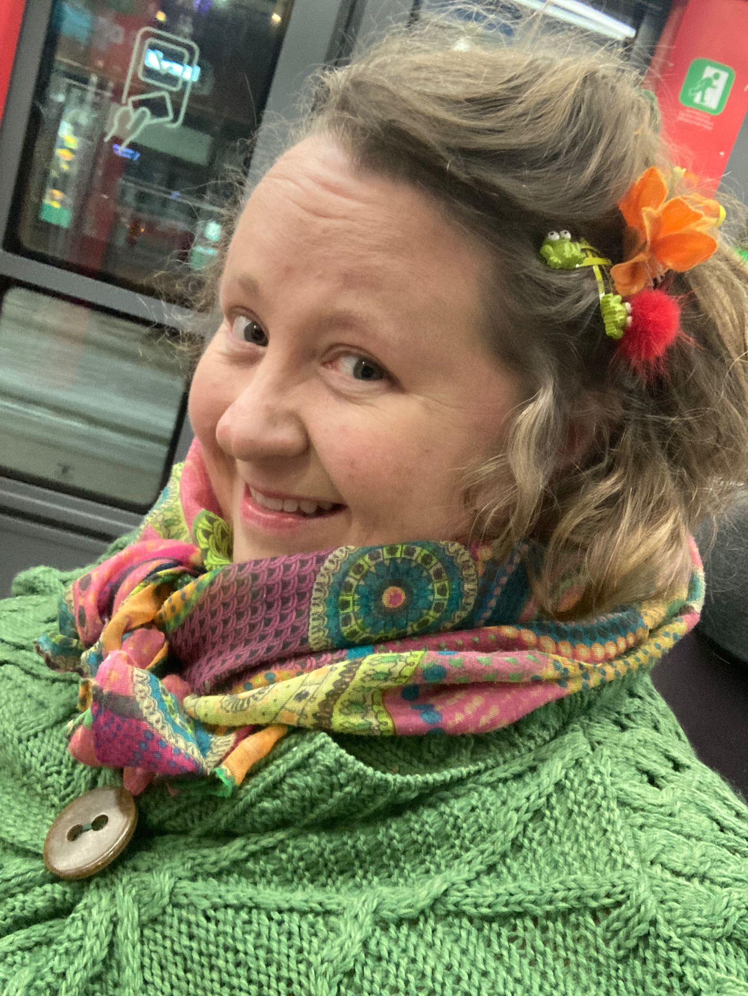 Värikkäisiin vaatteisiin ja asusteisiin pukeutunut Milla katsoo kujeilevasti kameraan. 